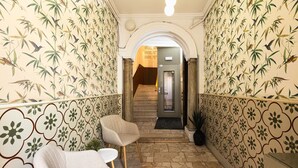 A hallway with patterned wallpaper, a staircase, and a seating area with a chair and a small table. - Hostal Vidamia (Málaga)