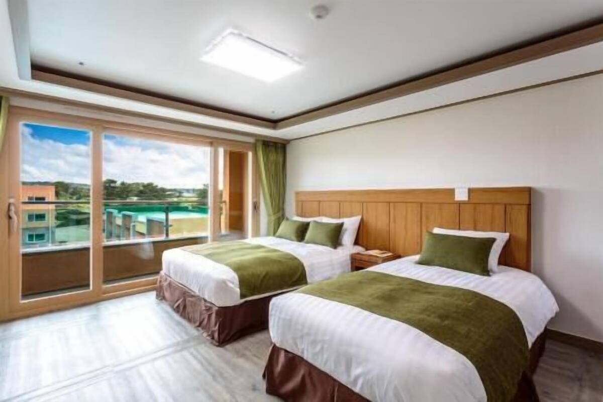 Une chambre d’hôtel avec deux lits, un balcon et une vue sur les bâtiments et la verdure.