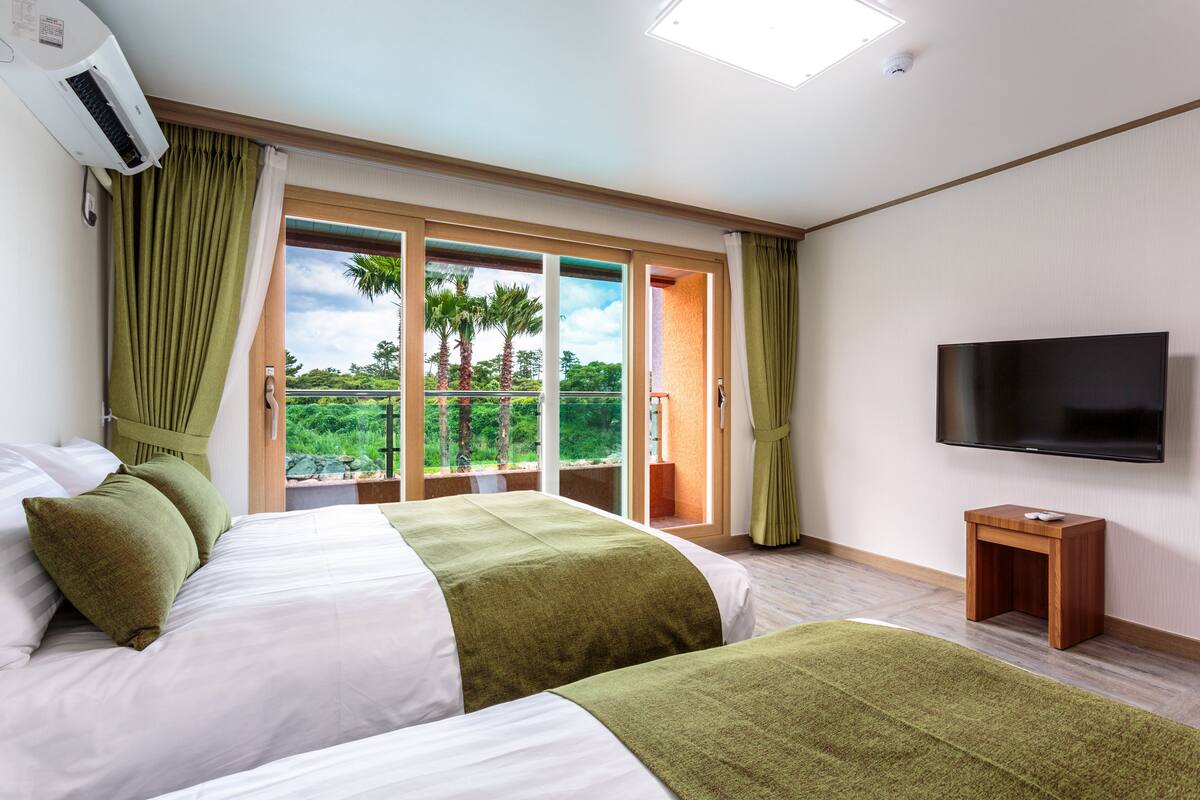 Une chambre d’hôtel avec un lit, une télévision et un balcon donnant sur des palmiers.