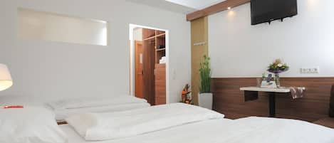 Habitación de hotel con dos camas, un televisor montado en la pared, una mesita con una planta y detalles decorativos de paneles de madera en la pared.