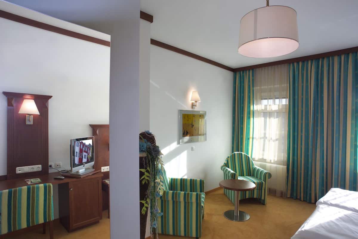 A hotel room with a bed, a desk with a computer, a chair, a small table, and a lamp.