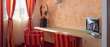 Habitación de hotel con alfombra roja, cortinas a rayas, un escritorio con computadora y una lámpara de pared.