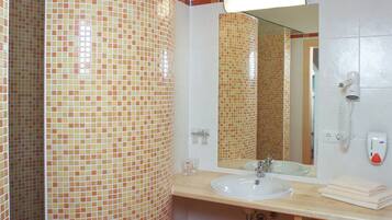 Un baño con pared de azulejos curvada, un lavamanos, un espejo, un secador de pelo y un perchero para toallas.