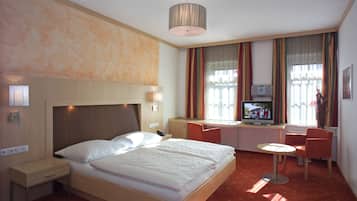 Une chambre d’hôtel comprenant un lit, une table de chevet, une lampe, une télévision, un bureau, une chaise et une petite table.