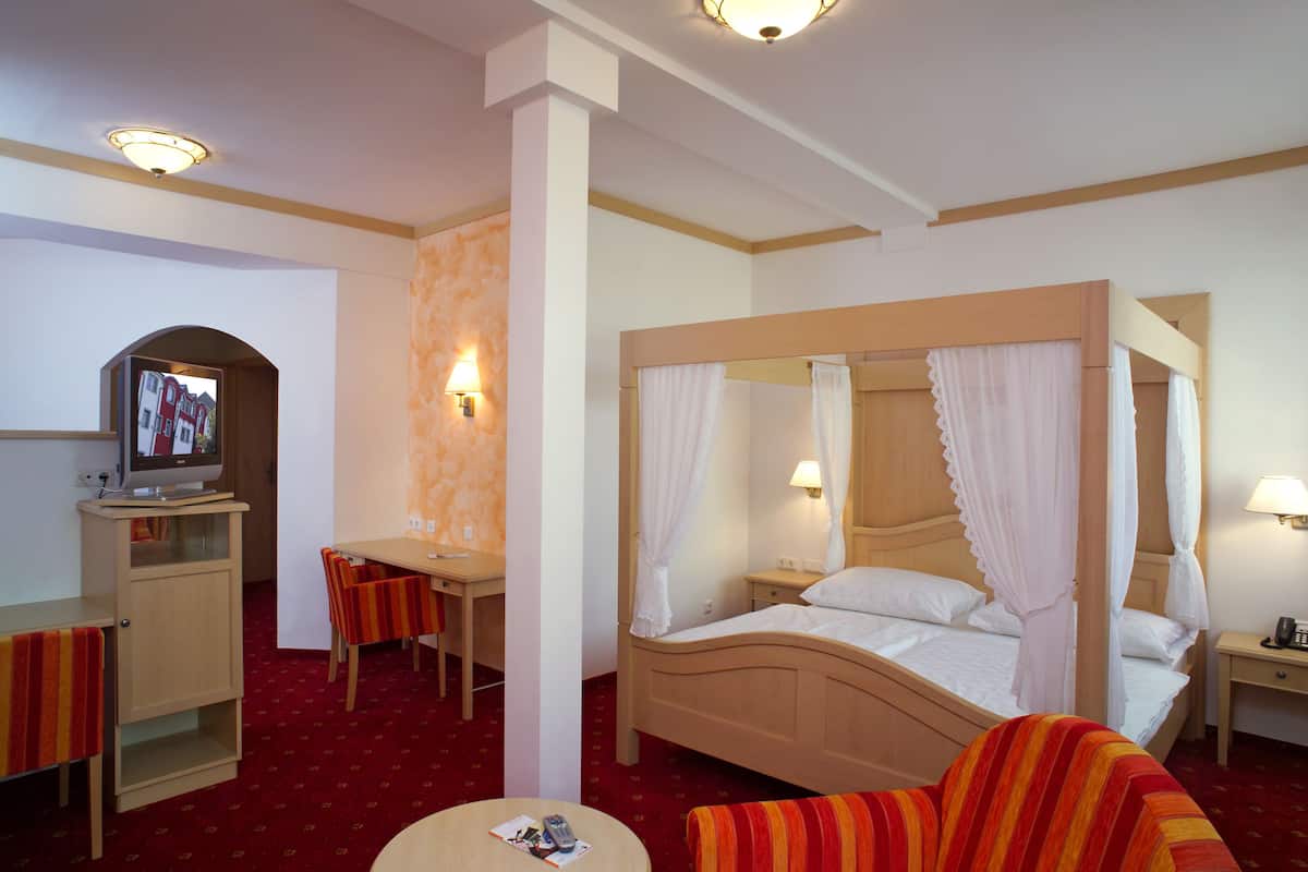 A hotel room with a four-poster bed, a desk with a chair, a television, and a small round table.