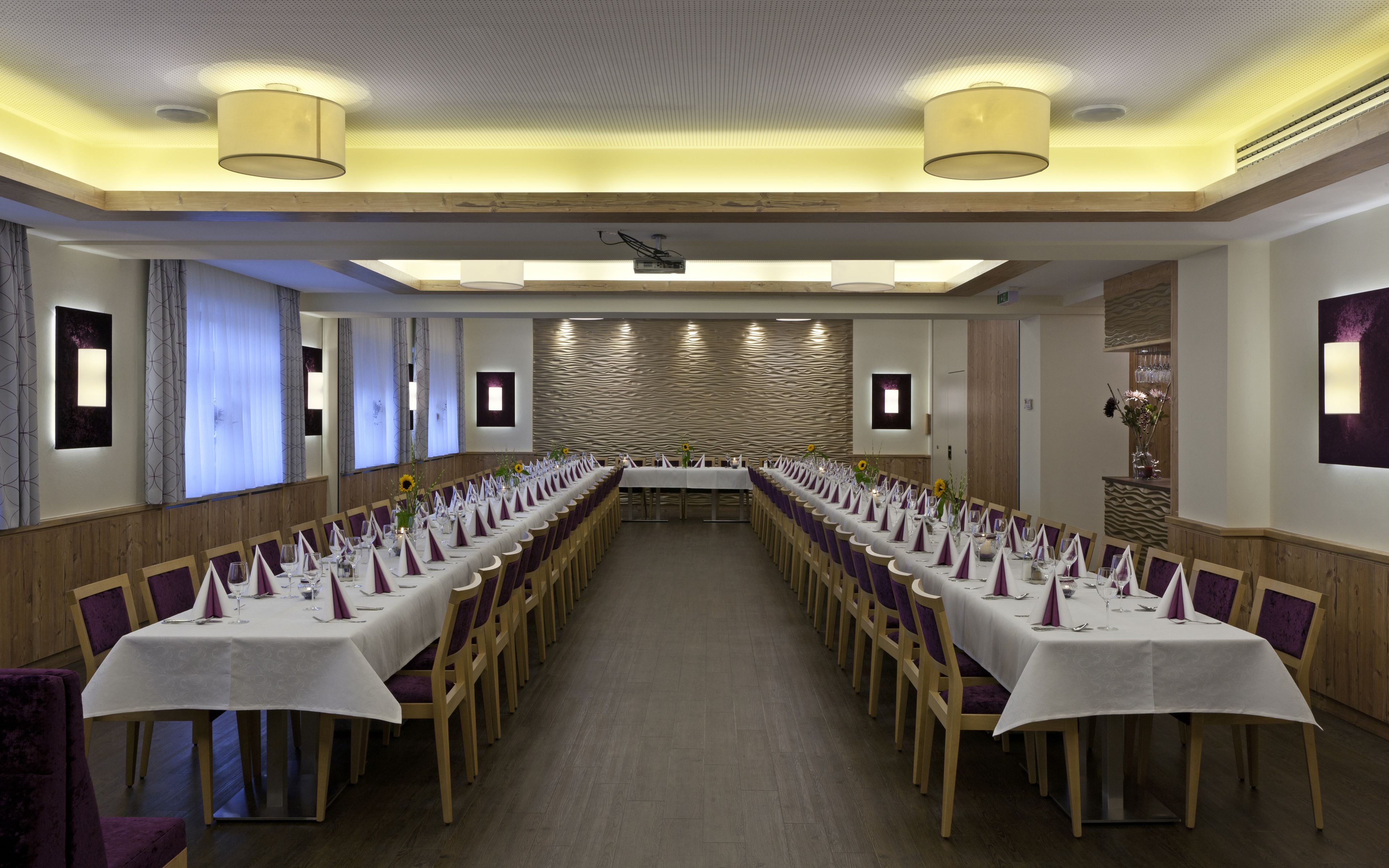 A conference room with long tables, purple chairs, and a modern ceiling design.