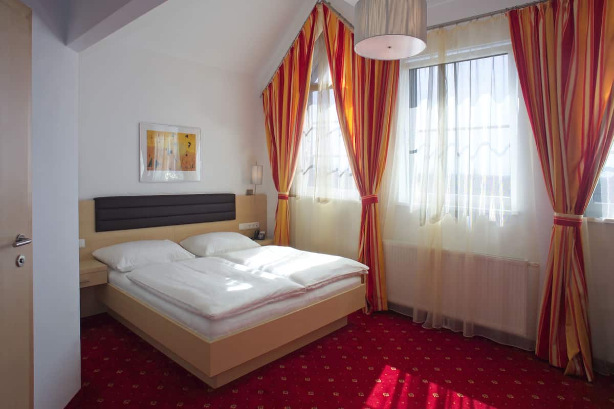 A hotel room with a bed, a headboard, a bedside table with a lamp, a framed picture on the wall, and curtains.