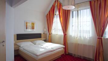 A hotel room with a bed, a headboard, a bedside table with a lamp, a framed picture on the wall, and curtains.