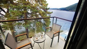 A balcony with a glass railing overlooking a lake, two chairs, a small round table with two cups, and a view of a forested hillside. - Abant Kosk (Mudurnu)