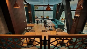 A restaurant with wooden tables and chairs, a green sofa, and large windows overlooking a body of water. - Abant Kosk (Mudurnu)