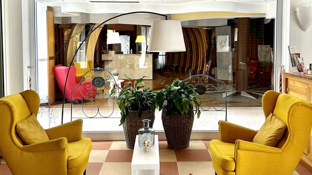 A modern living room with yellow armchairs, a white sofa, and a large window offering a view of a dining area. - Hotel Due Torri Tempesta (Noale)