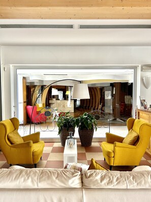 Un salon moderne avec des fauteuils jaunes, un canapé blanc et une grande fenêtre donnant sur un coin repas.