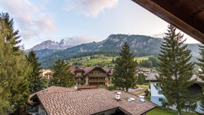 A mountain view with a building featuring a tiled roof and balconies. - Hotel Ramon (Campitello di Fassa)