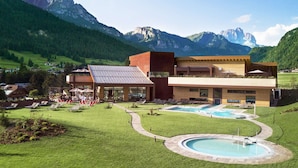 A modern hotel with a pool area, surrounded by lush green fields and mountains. - Hotel Ramon (Campitello di Fassa)