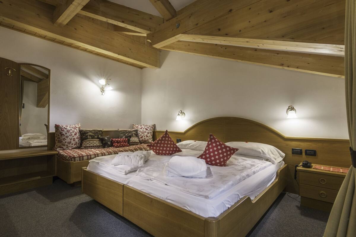 Ein Schlafzimmer mit Holzrahmen, ausgestattet mit einem großen Bett, Nachttischen, einem Spiegel und Wandleuchten.