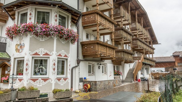 A traditional chalet with wooden balconies, flower boxes, and a stone facade. - Hotel Ramon (Campitello di Fassa)