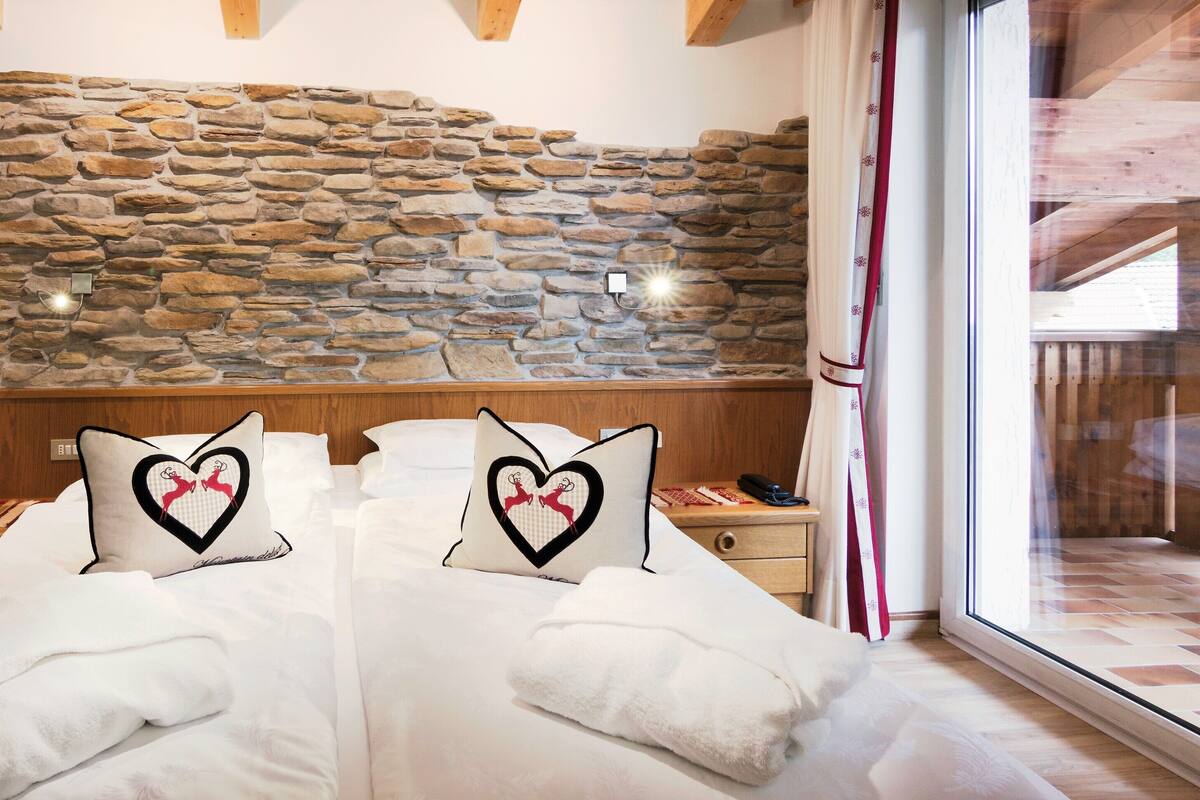 Ein Doppelbett mit zwei herzförmigen Kissen, eine Steinsäule, ein Holzkopfbrett, ein Nachttisch und ein Fenster mit Vorhängen.