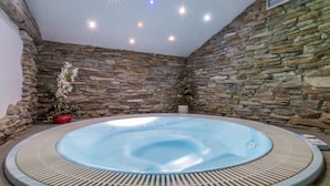 A hot tub in a stone-walled room with a ceiling light fixture. - Hotel Ramon (Campitello di Fassa)