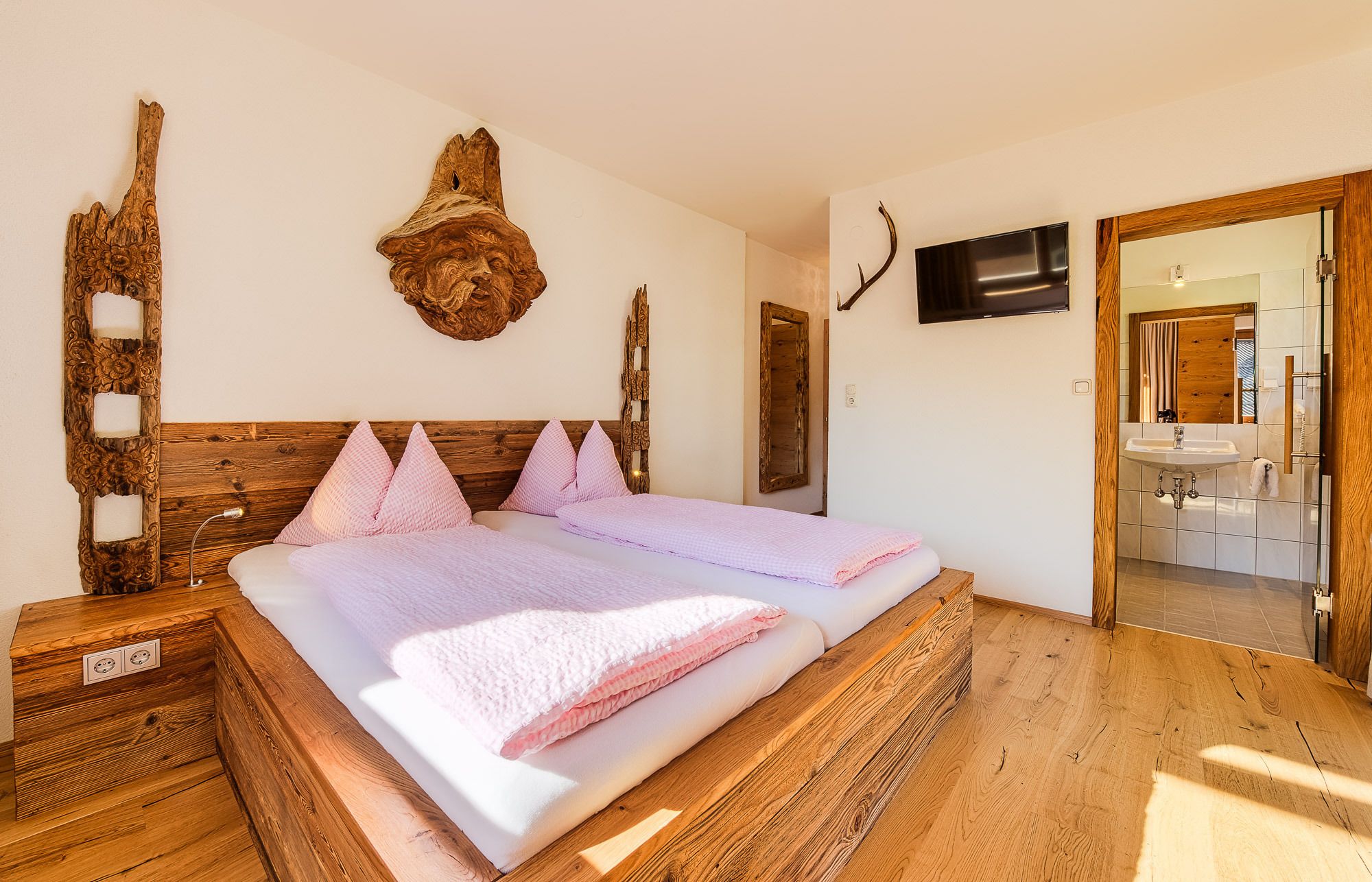Une chambre avec une tête de lit en bois, un grand miroir, un téléviseur à écran plat et un plancher en bois.