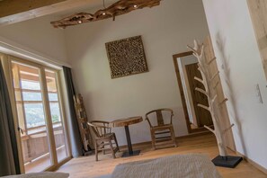 Una habitación con piso de madera, una mesa redonda con sillas, un adorno en la pared y un perchero de madera.