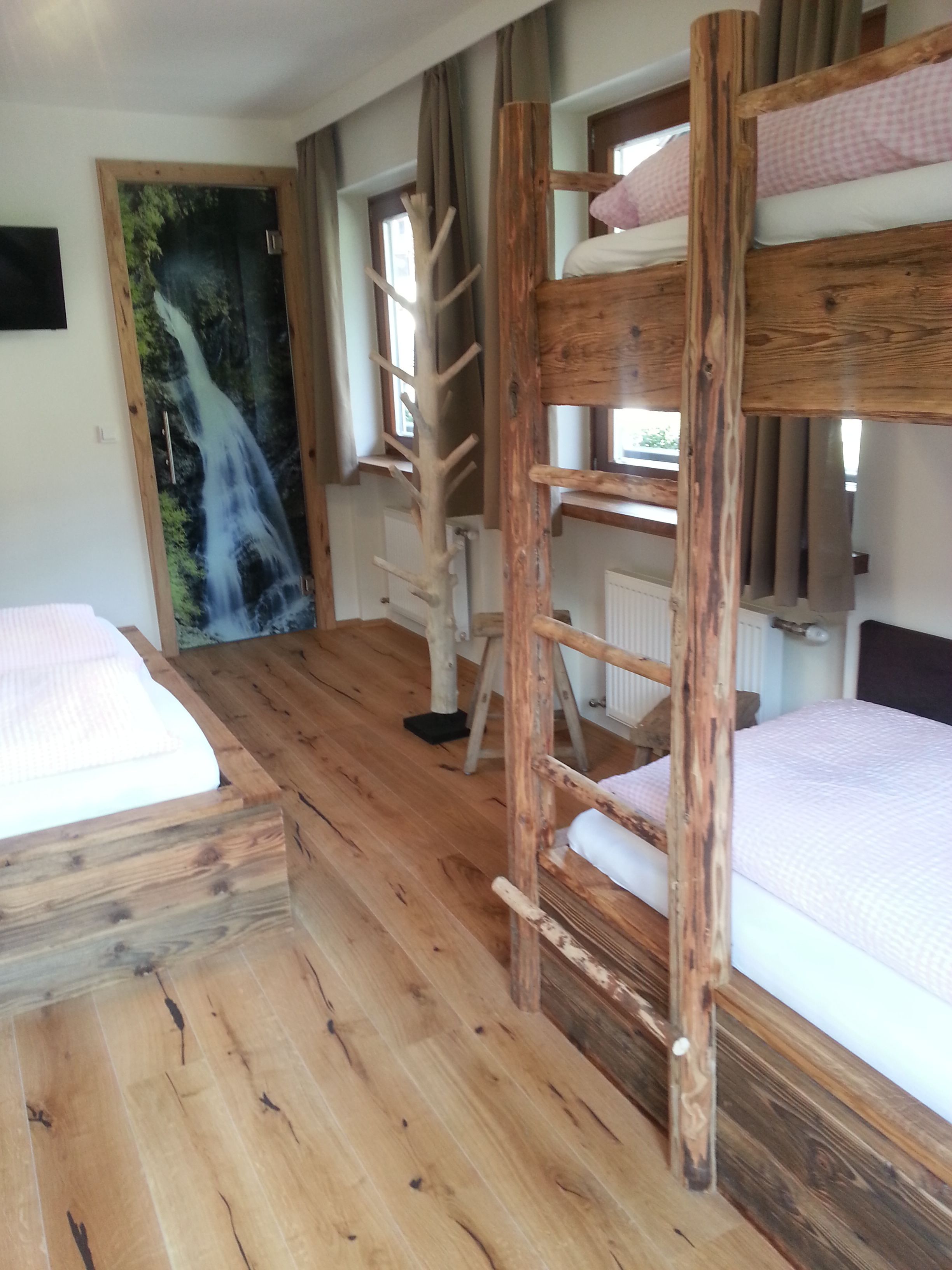 Een rustieke kamer met houten stapelbedden, een houten ladder en een muurschildering van een waterval.