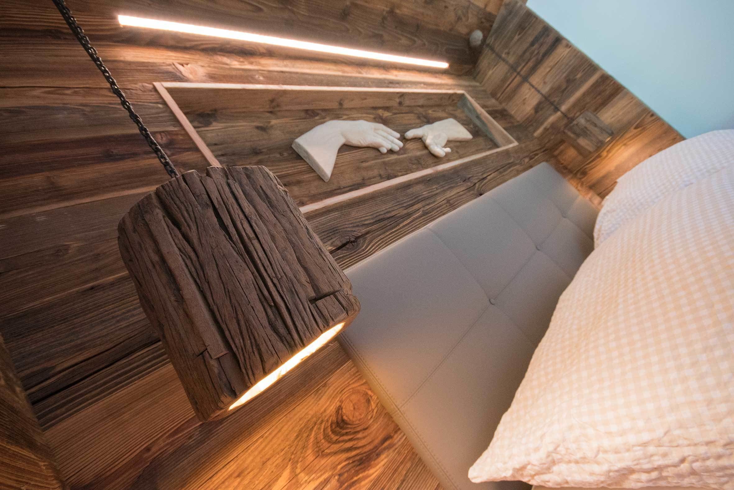 A wooden ceiling with a hanging light fixture and a bed with a white pillow.