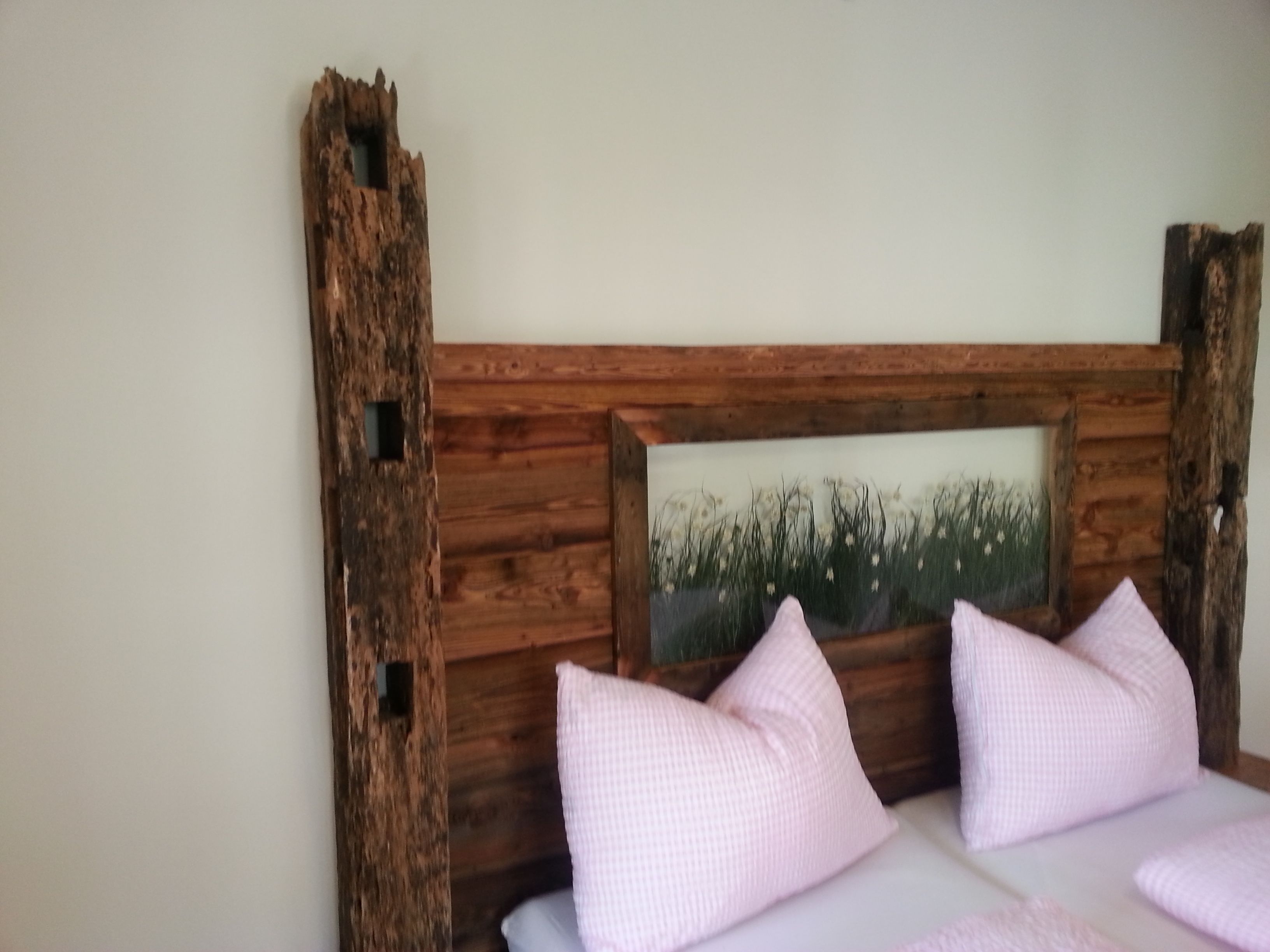 Un lit avec une tête de lit en bois, deux oreillers et un tableau représentant de l’herbe.