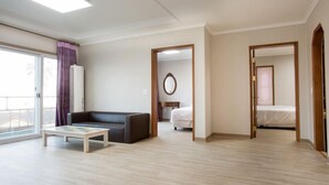 Una habitación amplia con un gran ventanal, un sofá, una mesita y una cama.