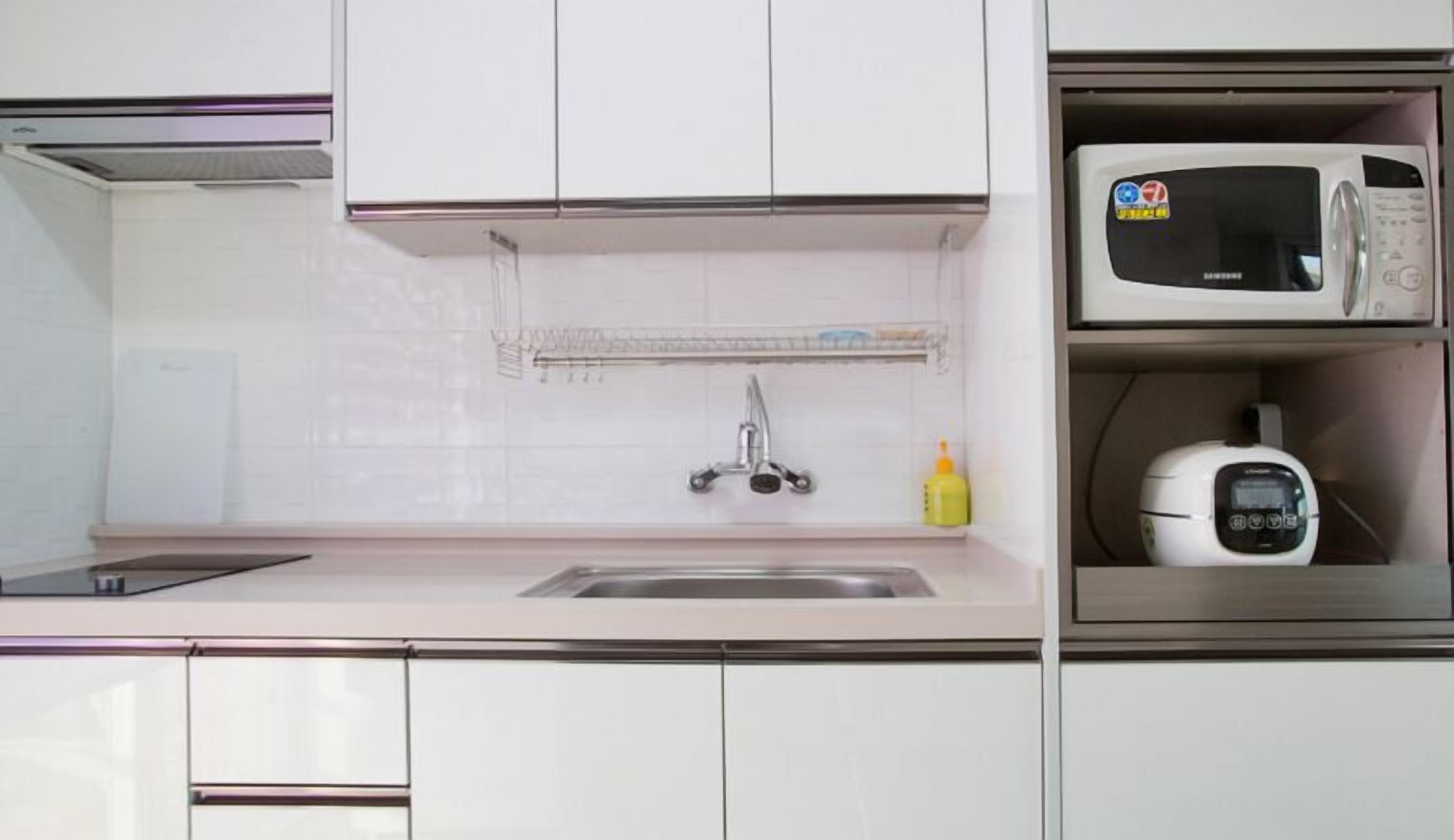 Una cocina con armarios blancos, un lavamanos de acero inoxidable, un microondas y una balanza digital.
