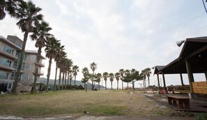 A grassy area with palm trees, a building with balconies, and a wooden structure with benches.