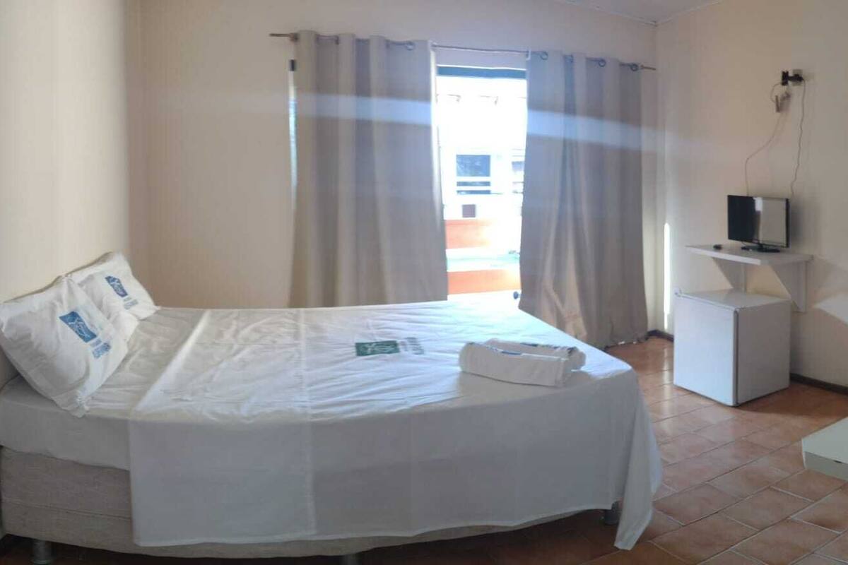 A single-bed room with a bed, a TV on a small stand, and a window with curtains.