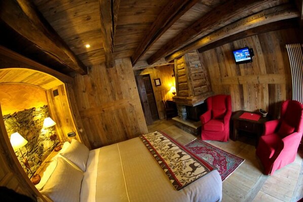Interior de una cabaña de madera con cama, sillas rojas, chimenea y televisor.
