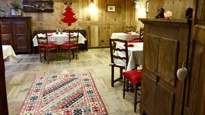 Ein rustikaler Essbereich mit Holzwänden und -decken, zwei für das Essen gedeckten Tischen und einem gemusterten Teppich auf dem Boden.
