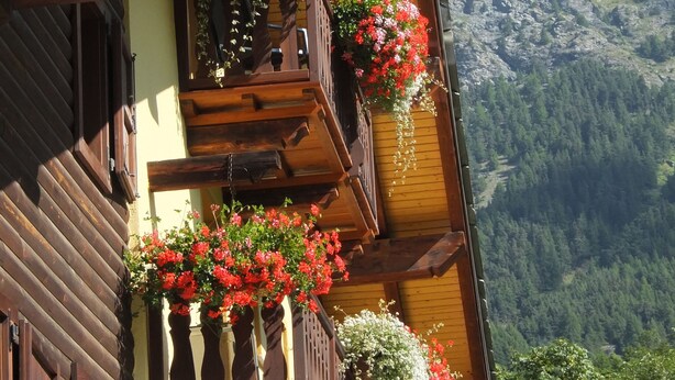Eine Holzhütte mit Balkonen, die mit Blumen geschmückt sind, vor einer Bergkulisse.