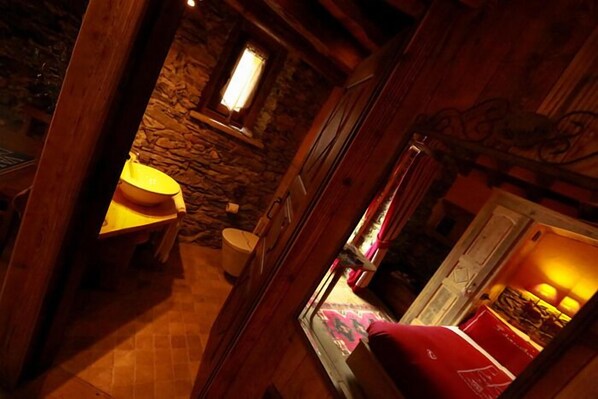 Una habitación acogedora con una pared de piedra, un banco de madera y una cama roja.