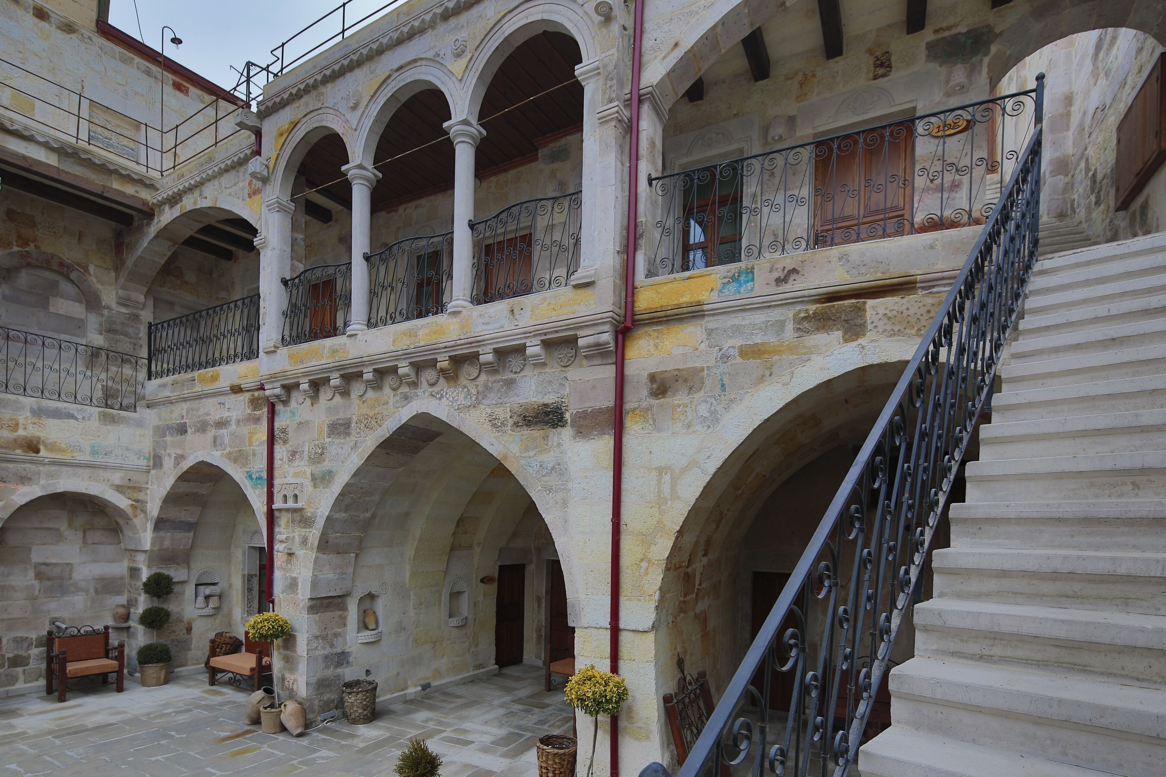 A courtyard with stone arches, a staircase, and a balcony with wrought iron railings.