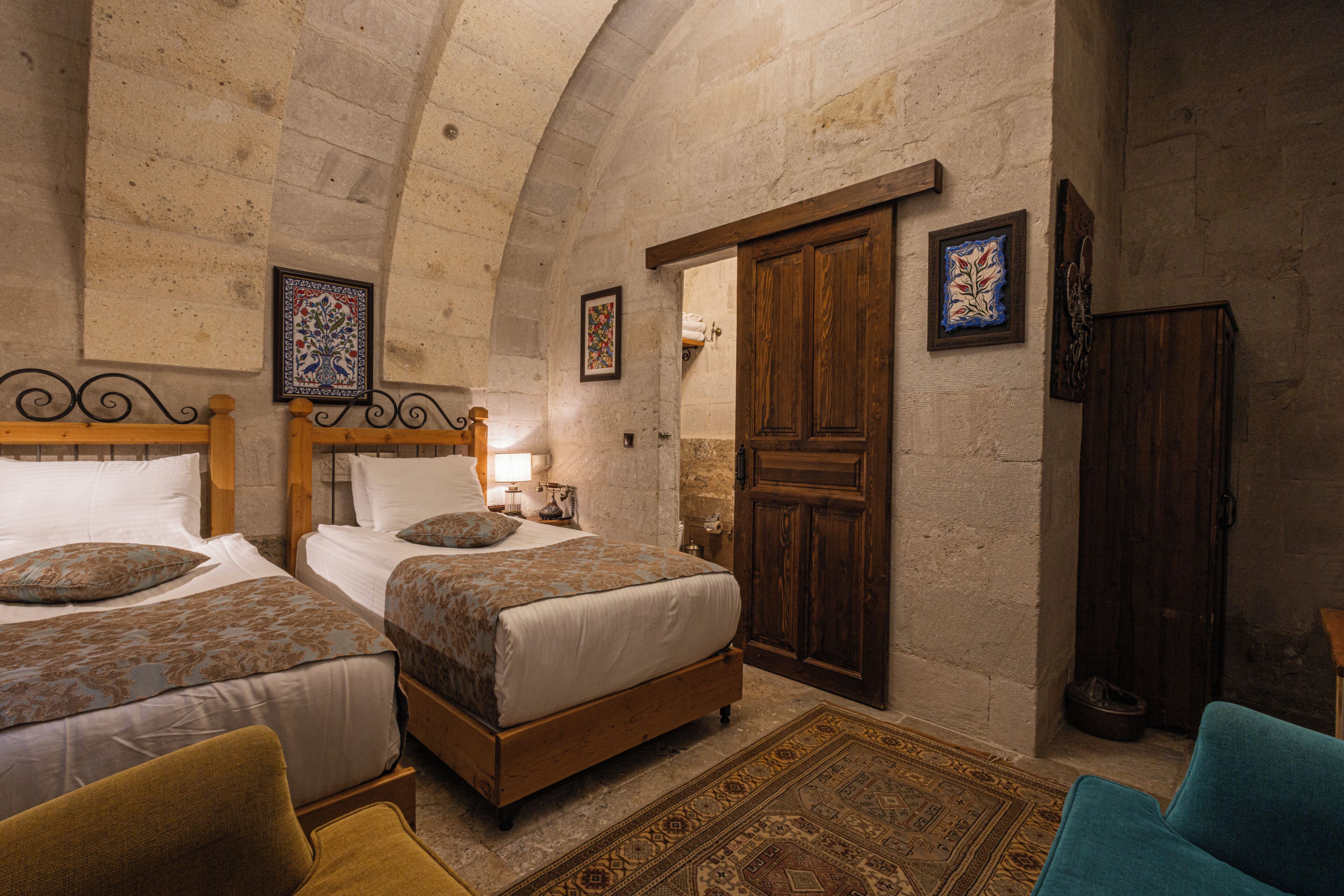 A room with two beds, a wooden wardrobe, and a large arched stone ceiling.