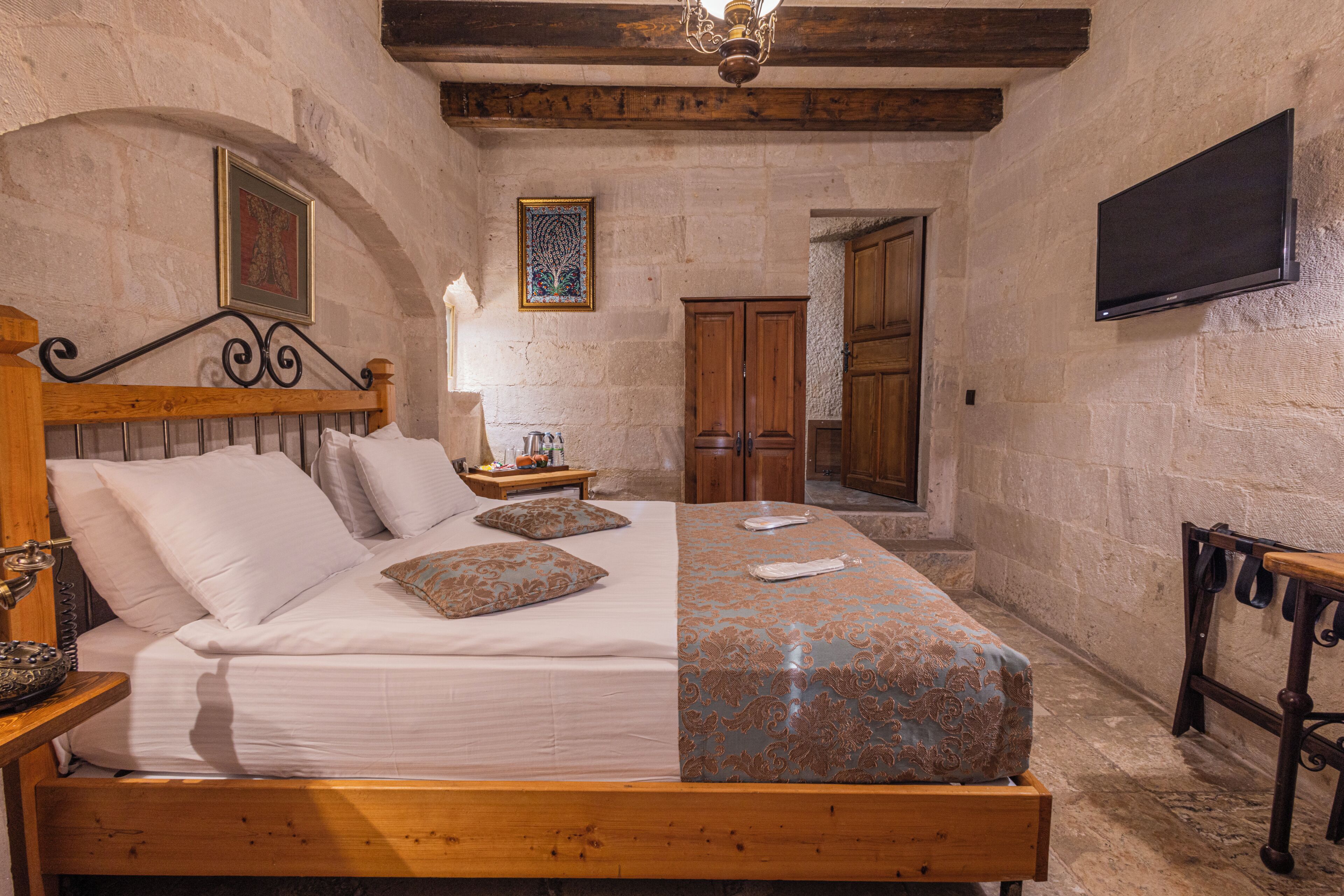 A bedroom with a wooden bed, a nightstand, a lamp, a TV, and a wooden door.