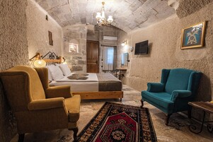 A cozy room with a bed, two armchairs, a chandelier, and a television.
