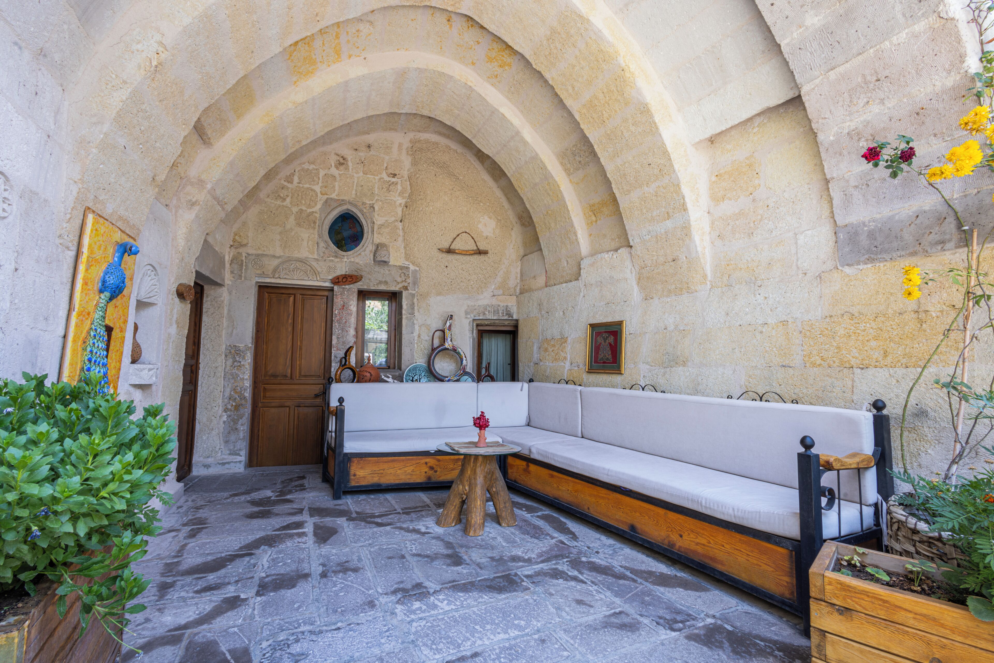 An interior with a stone archway, a wooden bench, a small table, and a sofa.