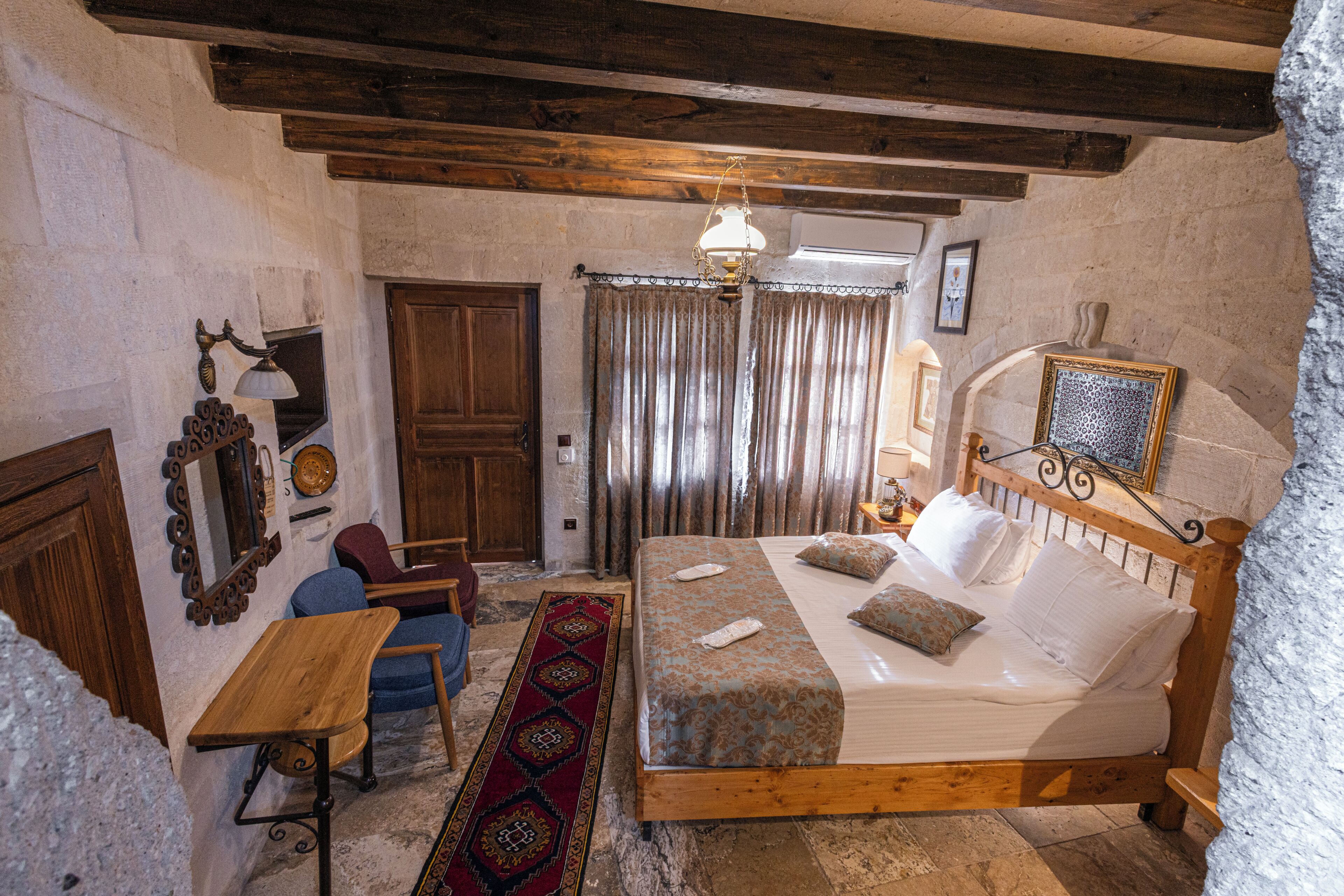 A traditional room with a wooden bed, a small table, a chair, a patterned rug, and a wooden ceiling.