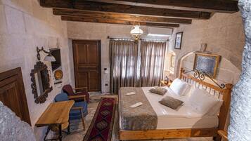 A traditional room with a wooden bed, a small table, a chair, a patterned rug, and a wooden ceiling.