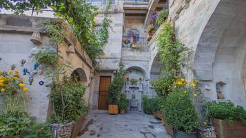 A narrow stone courtyard with a wooden door, potted plants, and hanging baskets.