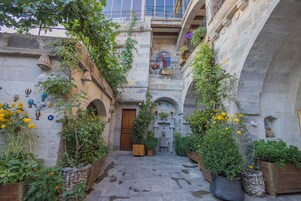 Un estrecho patio de piedra con una puerta de madera, plantas en macetas y cestas colgantes.