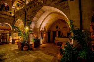 An interior courtyard with stone arches, potted plants, and a wooden bench.