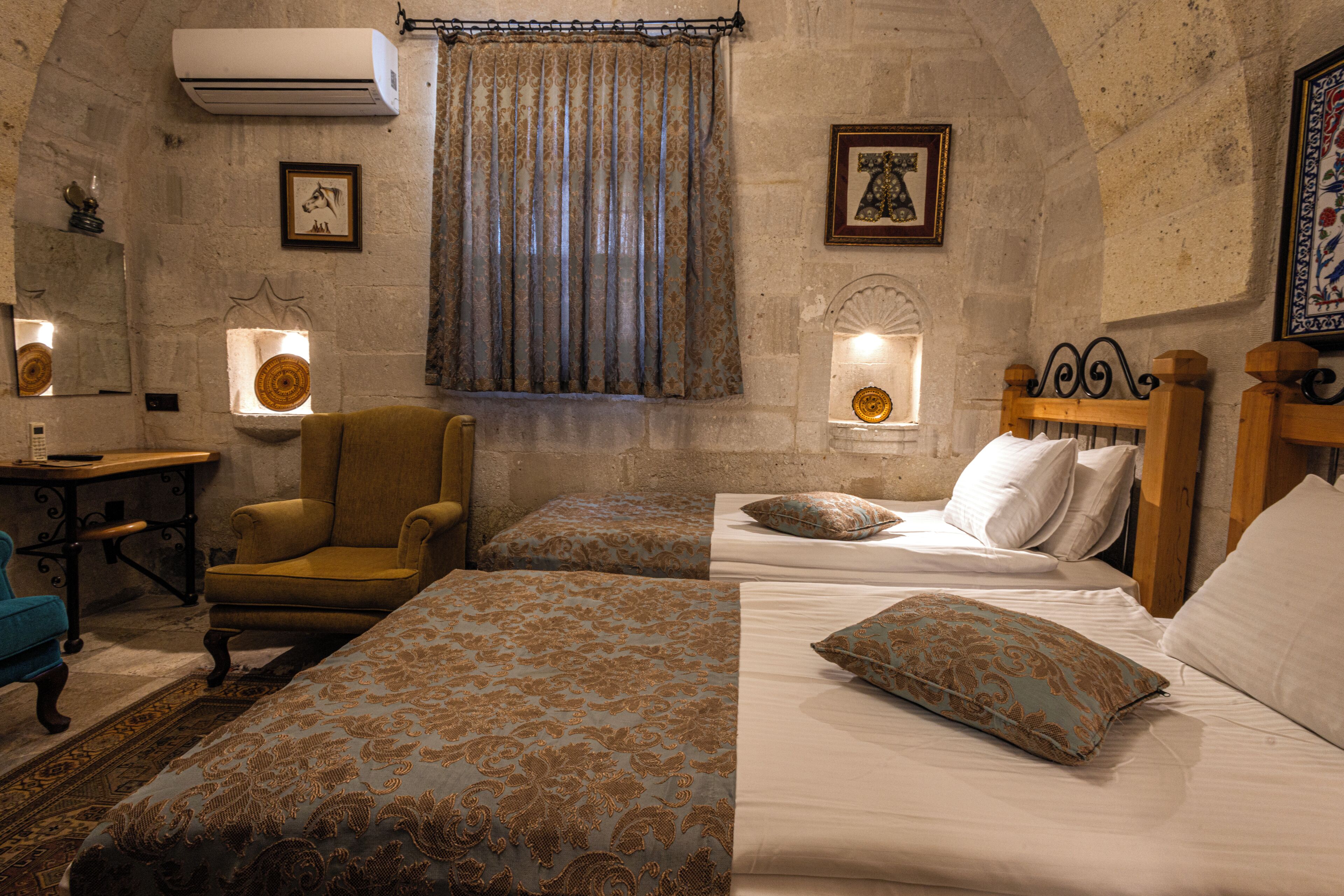 A room with two beds, a chair, a desk, and a wall-mounted air conditioner.