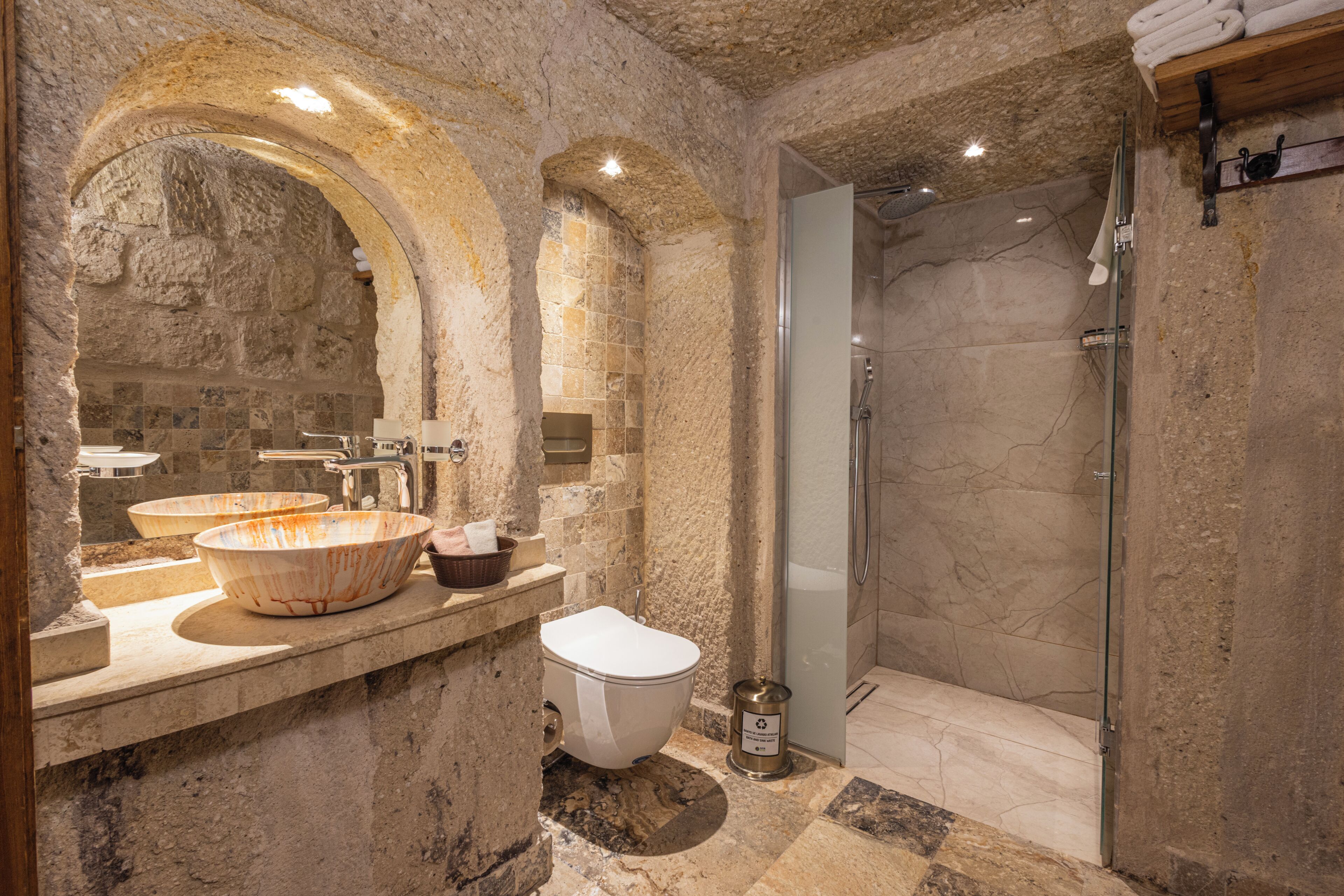 Ein Badezimmer mit Steinwand, großem Waschbecken, Toilette und Duschbereich.