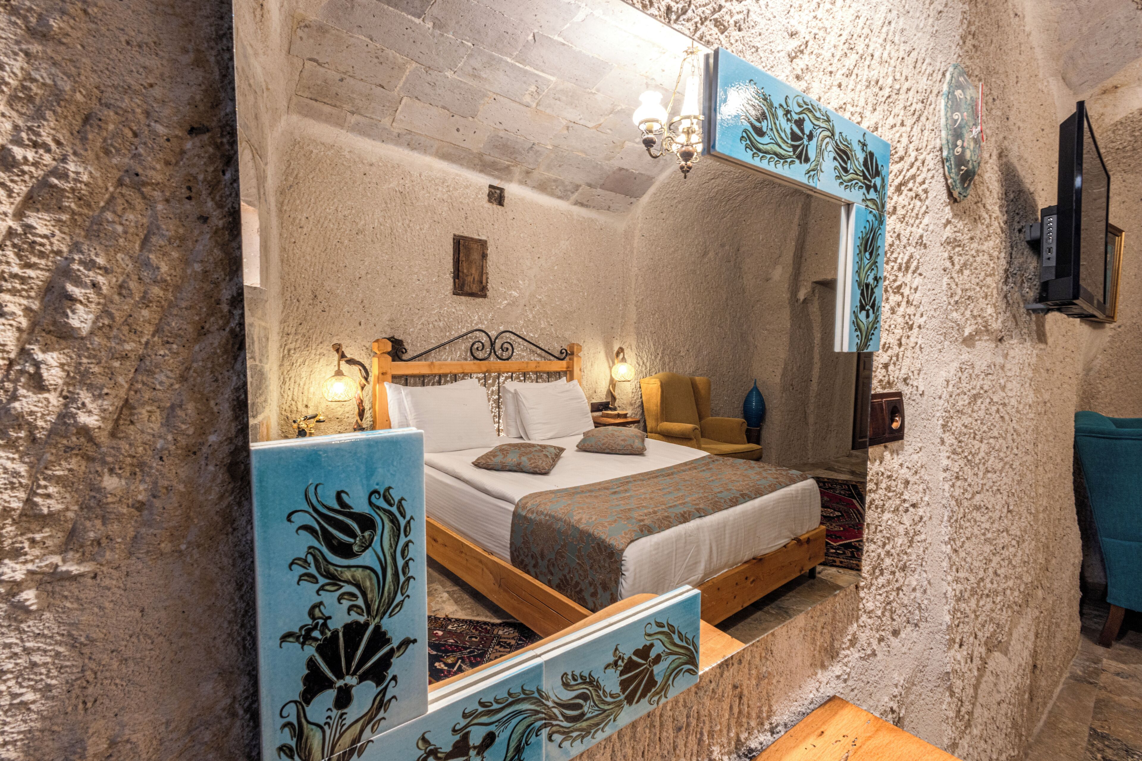 A bedroom with a stone wall, a bed with a wooden frame, a nightstand, a chair, and a mirror.