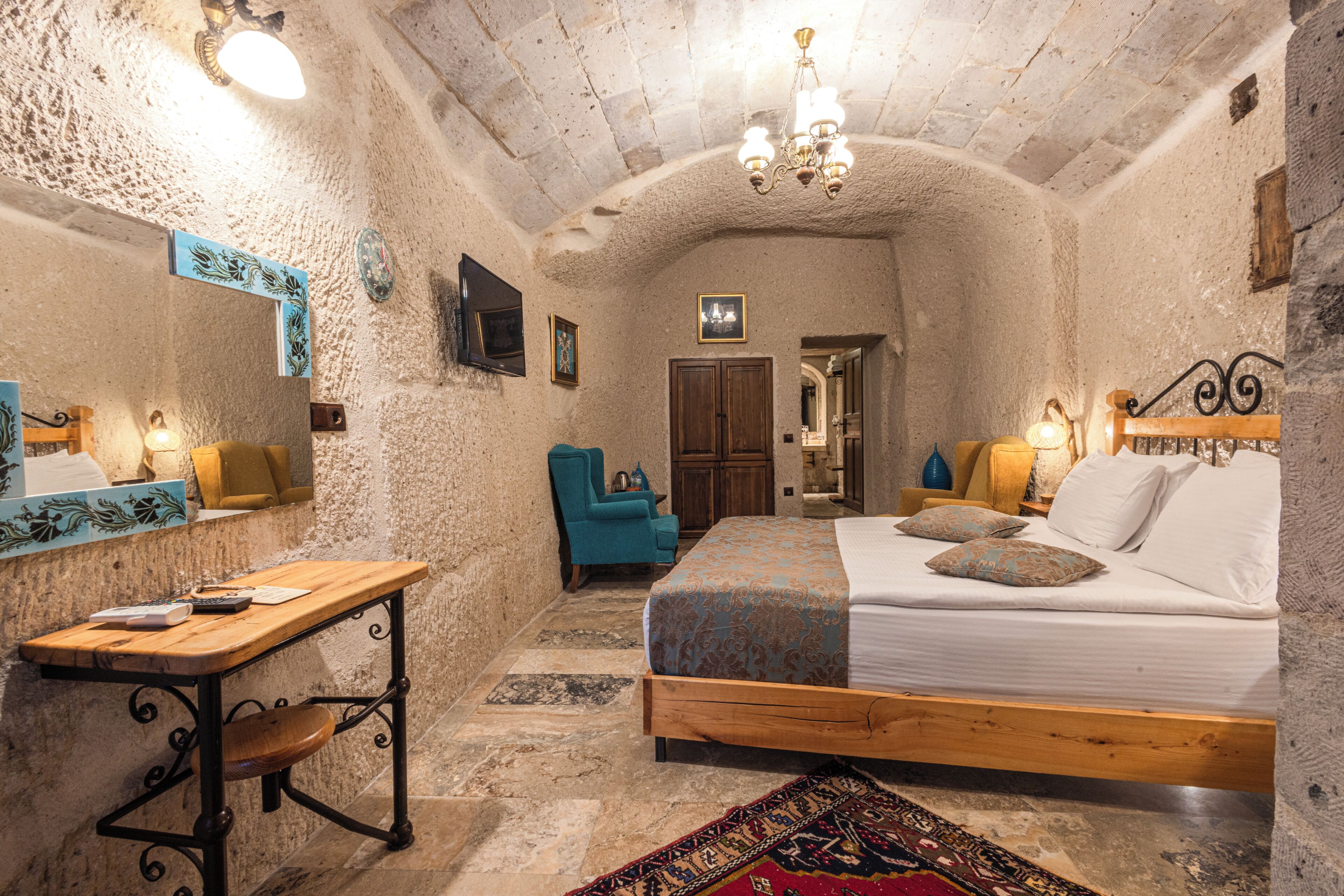 A cozy room with a bed, a desk, and a chair. There is a chandelier hanging from the ceiling.