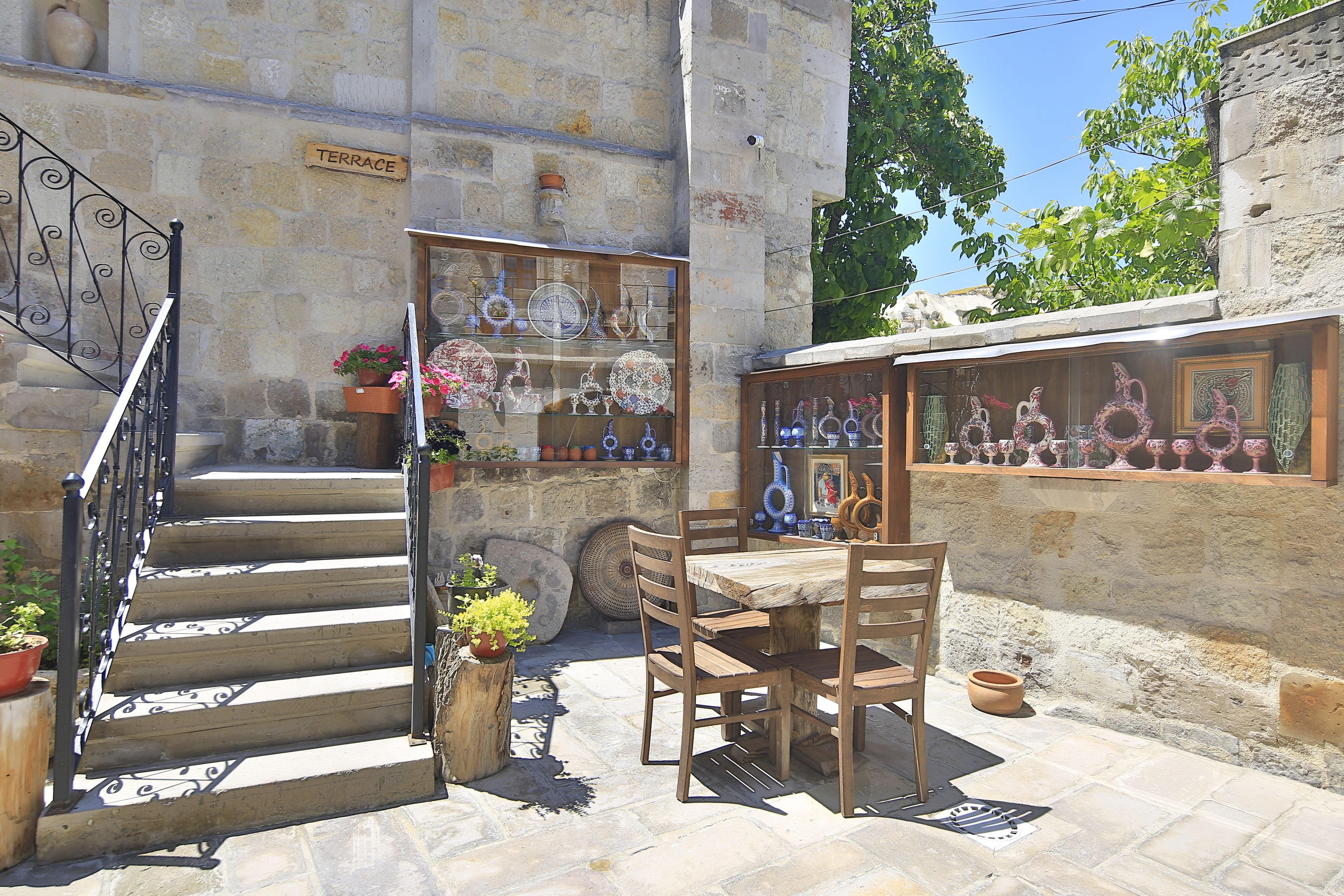 A stone staircase leading to a terrace with a wooden table and chairs, surrounded by potted plants and decorative items.